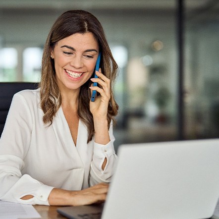 Smiling woman talking on phone and working on laptop