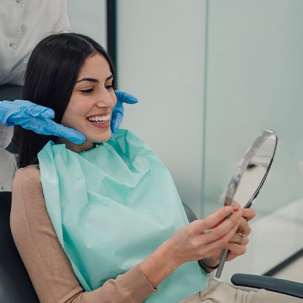Woman smiling at reflection in handheld mirror