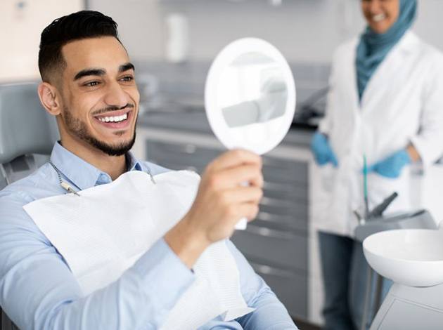 Cosmetic dentistry patient holding mirror, looking at his smile