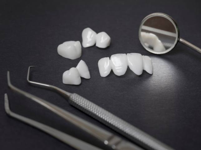 Several white dental crowns and veneers on table with dental instruments