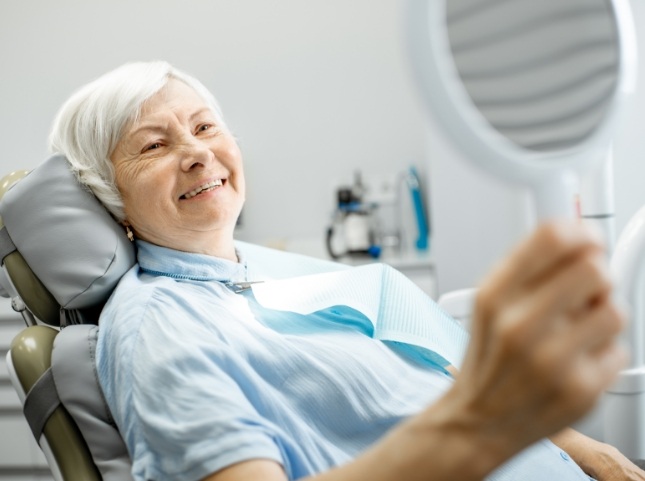 Senior dental patient admiring her smile in mirror