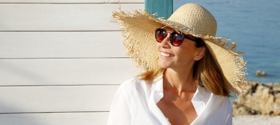 Smiling woman in sunhat and sunglasses sitting outdoors