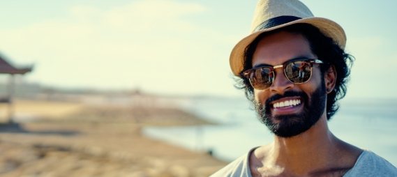 Man in fedora and sunglasses smiling on the beach