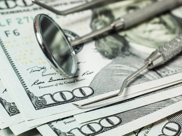 Dental tools laying on a pile of hundred-dollar bills