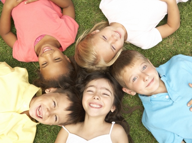 Group of smiling children laying in grass with their heads forming a circle