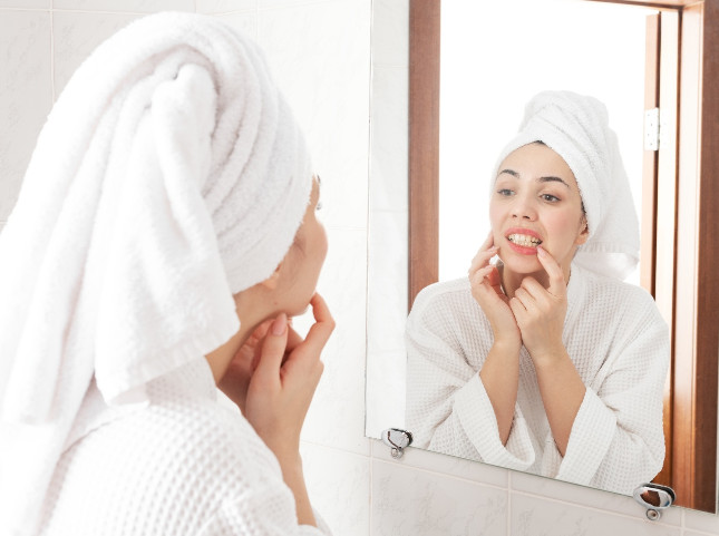 Woman in white robe looking at gums in reflection