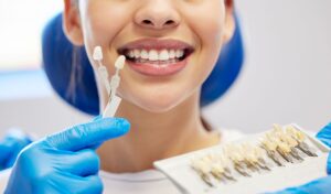 Nose-to-shoulder view of woman smiling with hand holding shade guide to her teeth